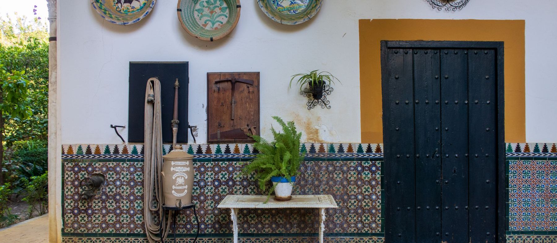Patio sevillano encalado con zócalo de azulejos, puerta de madera y platos de cerámica